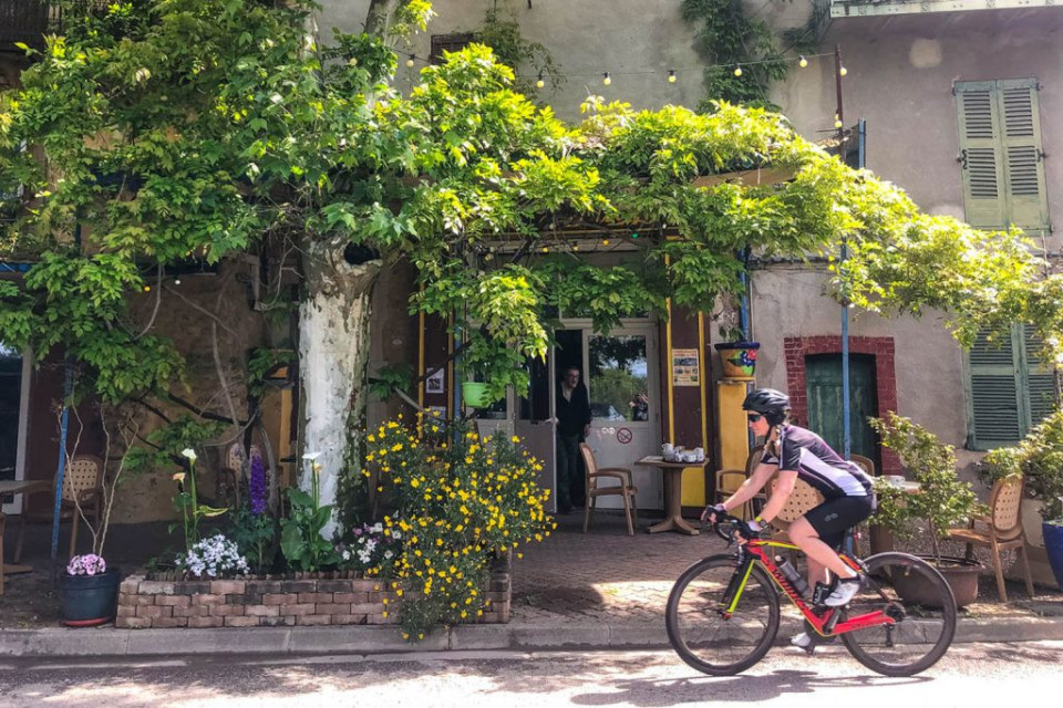 Cyclist passing colourful French cafe on Marmot Tours guided road cycling tour Mont Ventoux Provence France