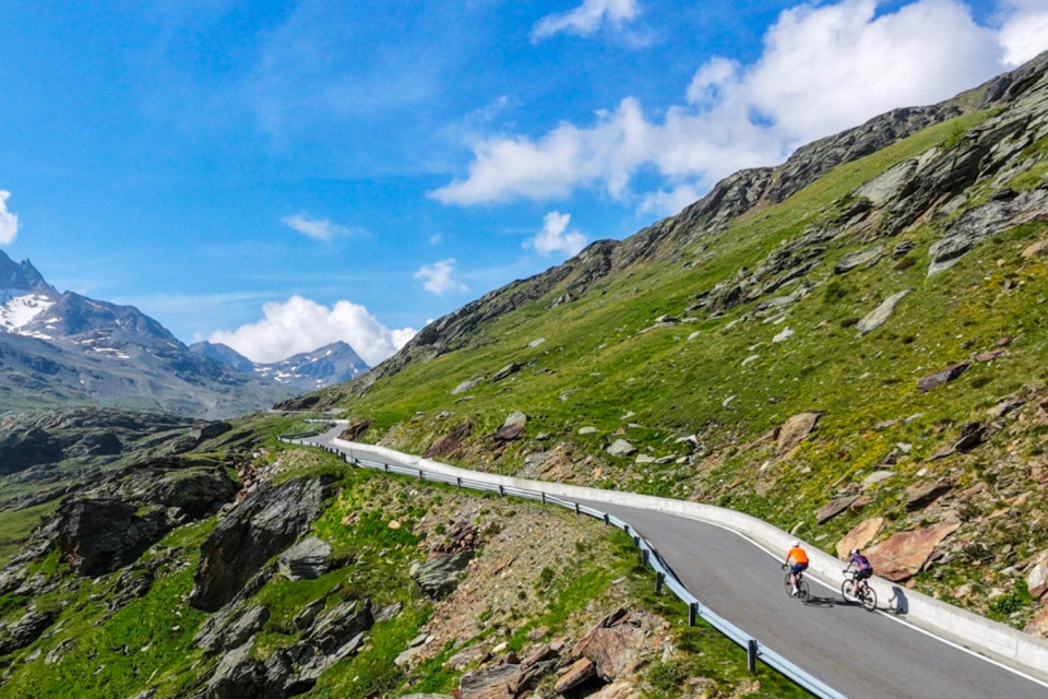 pair of cyclists climb Passo di Gavia alongside mountain peaks on marmot tours guided road cycling holiday dolomites