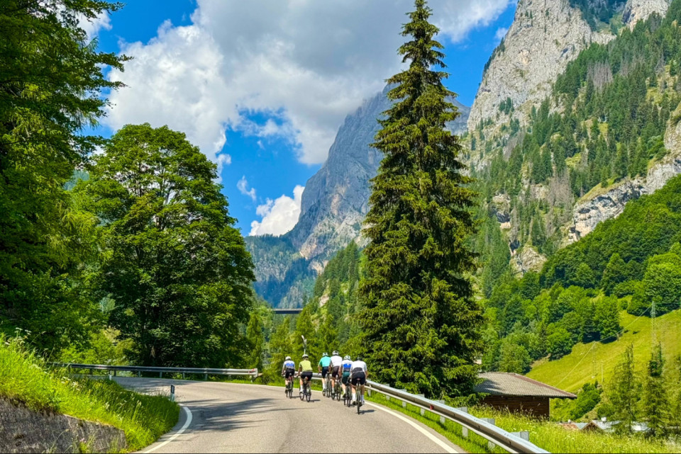 Group of cyclists climb passo di Fedaia climb alongside limestone peaks of dolomites on marmot tours cycling holiday