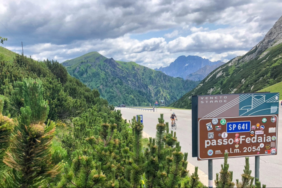 cyclist summiting passo di Fedaia approaching pass sign on Italian dolomites cycling holiday with marmot tours