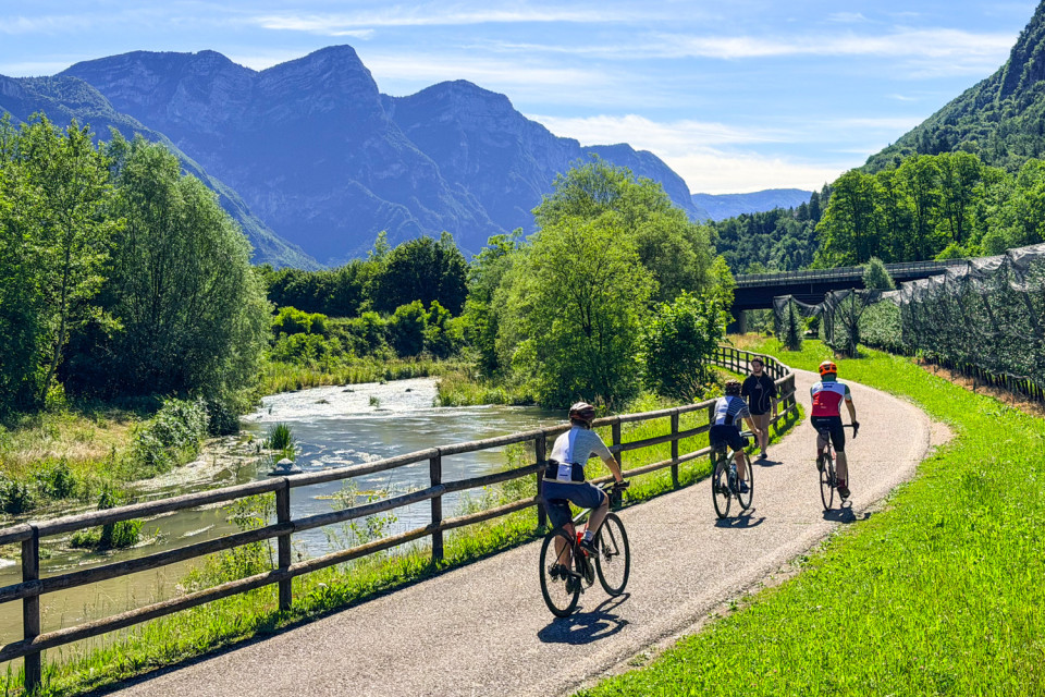 Group of cyclists climbing passo manghen Italian dolomites passing river and mountain peaks