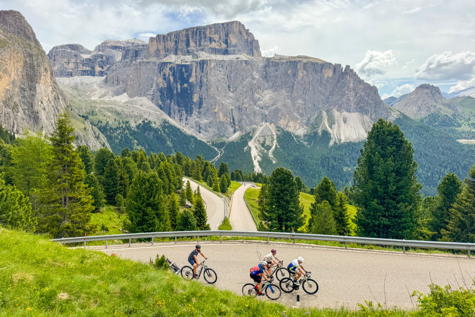 cyclists climbing passo sella with huge dolomites peak backdrop on marmot tours ultimate dolomites cycling holiday