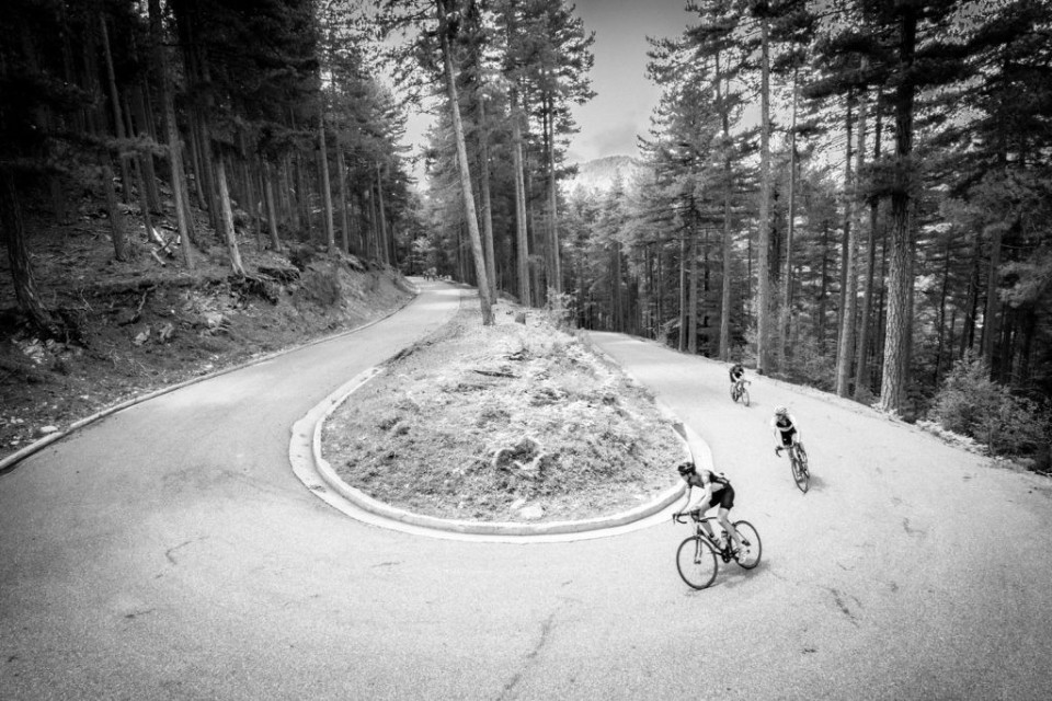 Black and white image of cyclists rounding hairpin bend in forest climbing Col de Verde on Marmot Tours Raid Corsica road cycling holiday