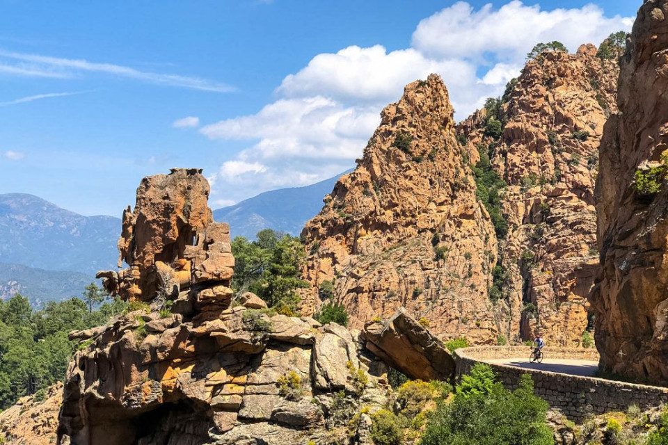 Cyclist riding through stunning rocky cliffs of Les Calanches on Raid Corsica with Marmot Tours road cycling holidays