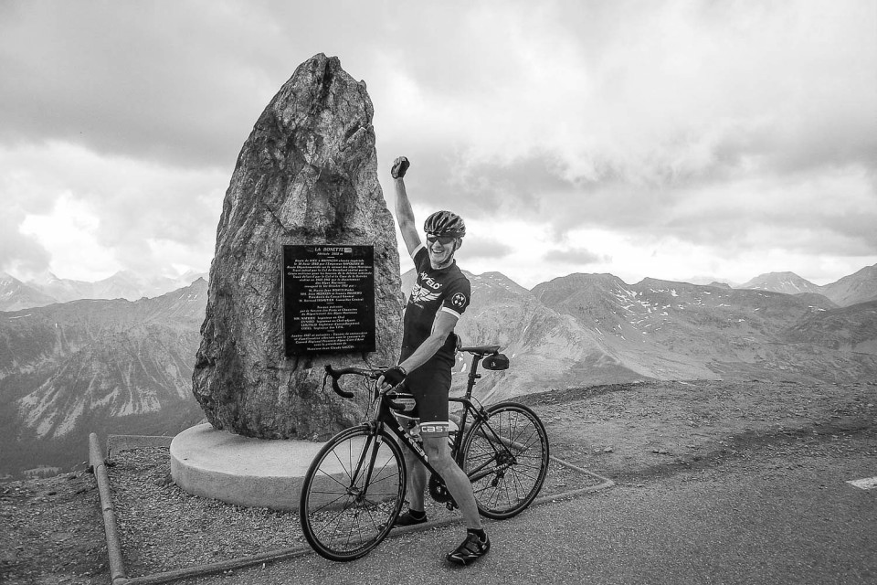 Black and white image of cyclist celebrating at Cime de la Bonette on Marmot Tours Raid Alpine cycling challenge