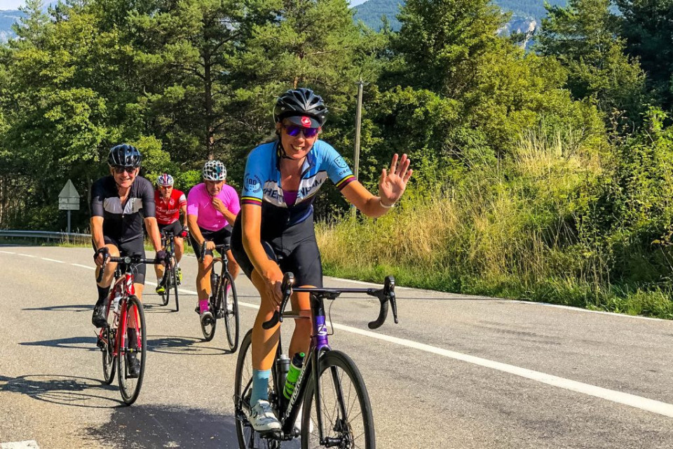 Group of cyclists smiling and waving while climbing on Day 6 of Marmot Tours Raid Alpine cycling challenge French Alps