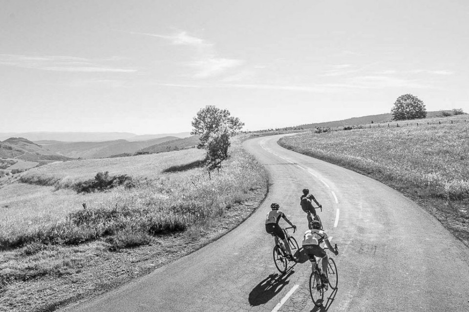 Black and white image of 3 cyclists on road in open moorland on Marmot Tours Raid du Massif Central France cycling holidays