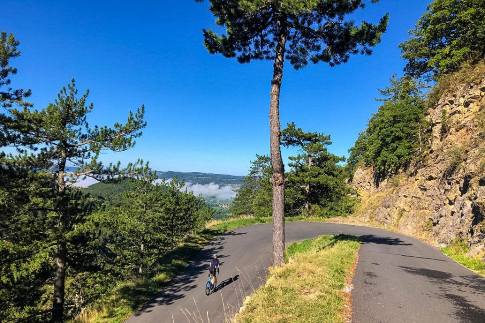 Cyclist climbing hairpin bend in sunshine on mountain road marmot Tours Raid Massif Central French cycling holiday
