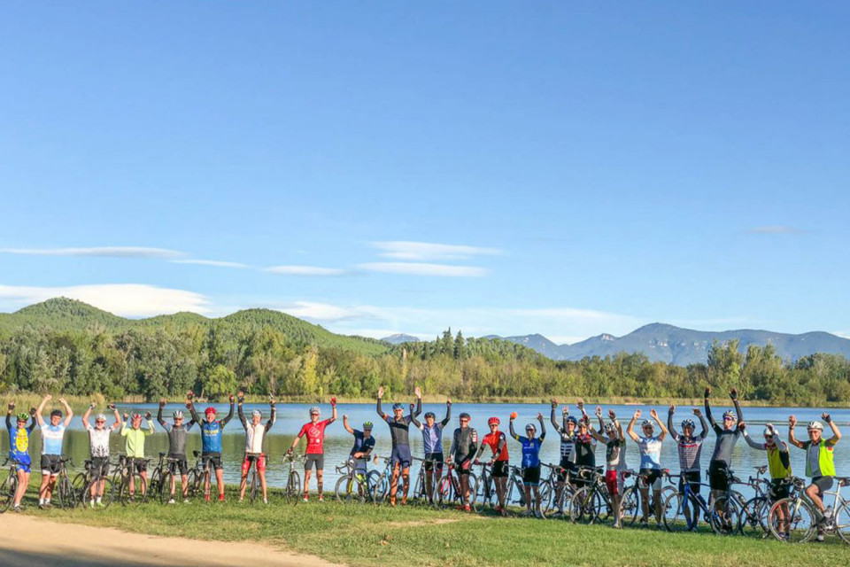 Group of cyclist raise hands cheering on shore of Lake Bangles on Catalonia cycling tour with Marmot Tours