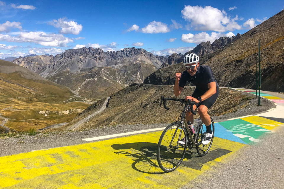 cyclist summiting col du Galibier riding over Tour de France painted road with mountain peaks in distance on marmot tours guided road cycling holiday French alps