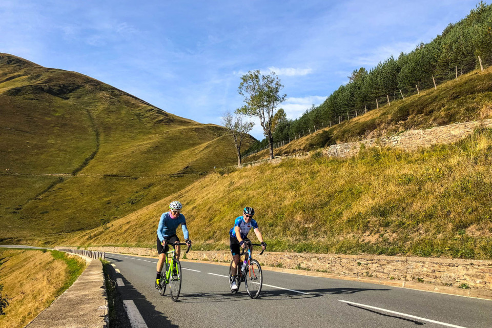 pair of cyclists climb green slopes of col de peyresourde on pyrenees Atlantic to mediterranean cycling challenge with marmot tours
