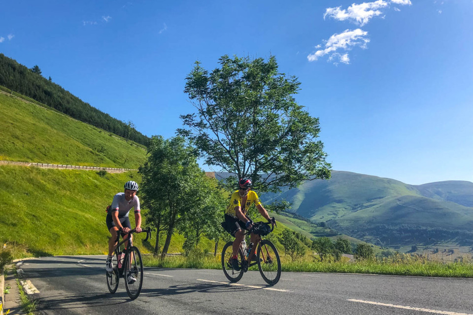 pair of cyclists climbing col de peyresourde with green mountain slopes and blue sky on French pyrenees road cycling holiday with marmot tours