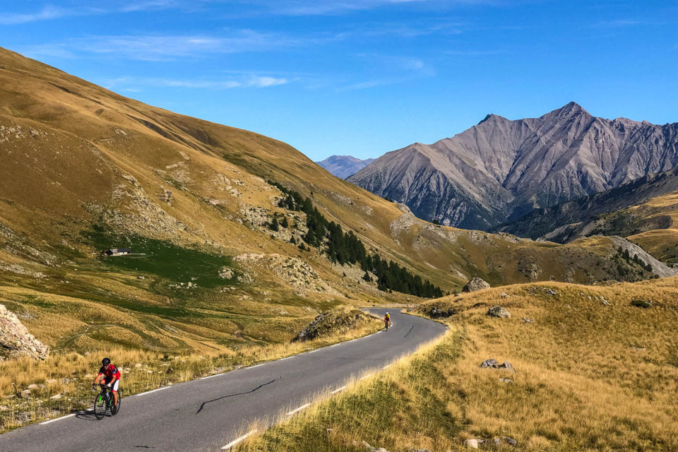 cyclist clime cime de la bonnette with vast alpine backdrop on marmot tours road cycling holiday French alps