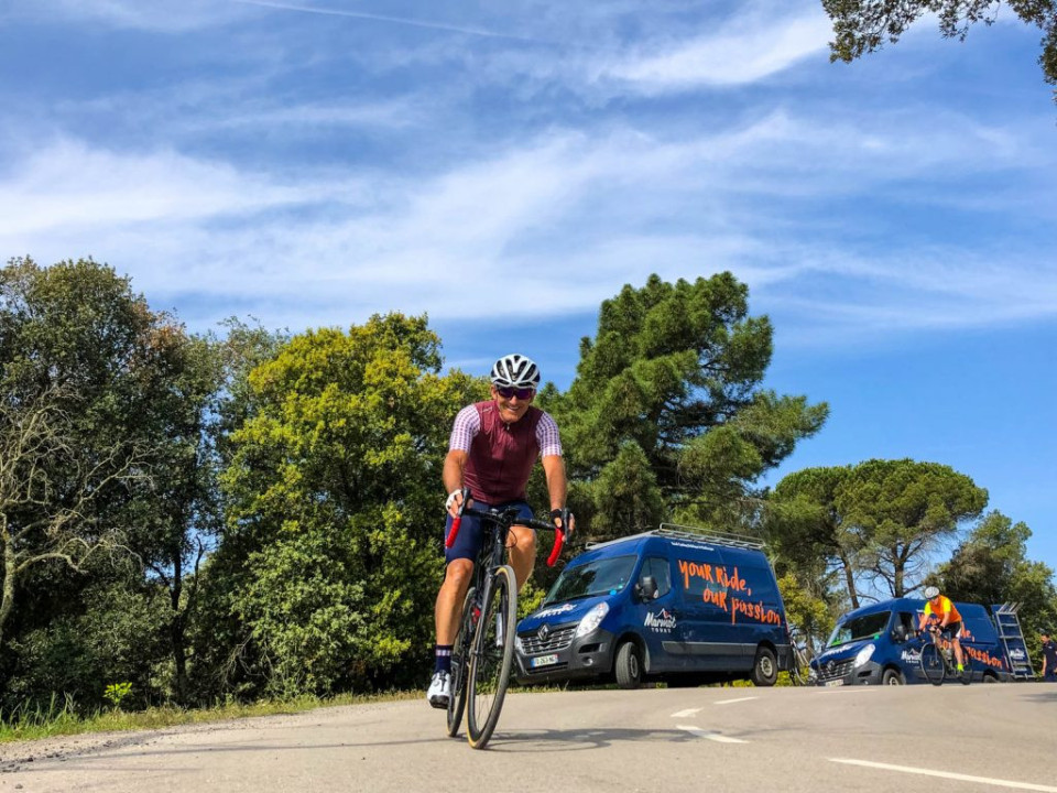 Cyclist enjoying support of two support vehicles on Marmot Tours guided road cycling tour of Girona Catalonia Spain