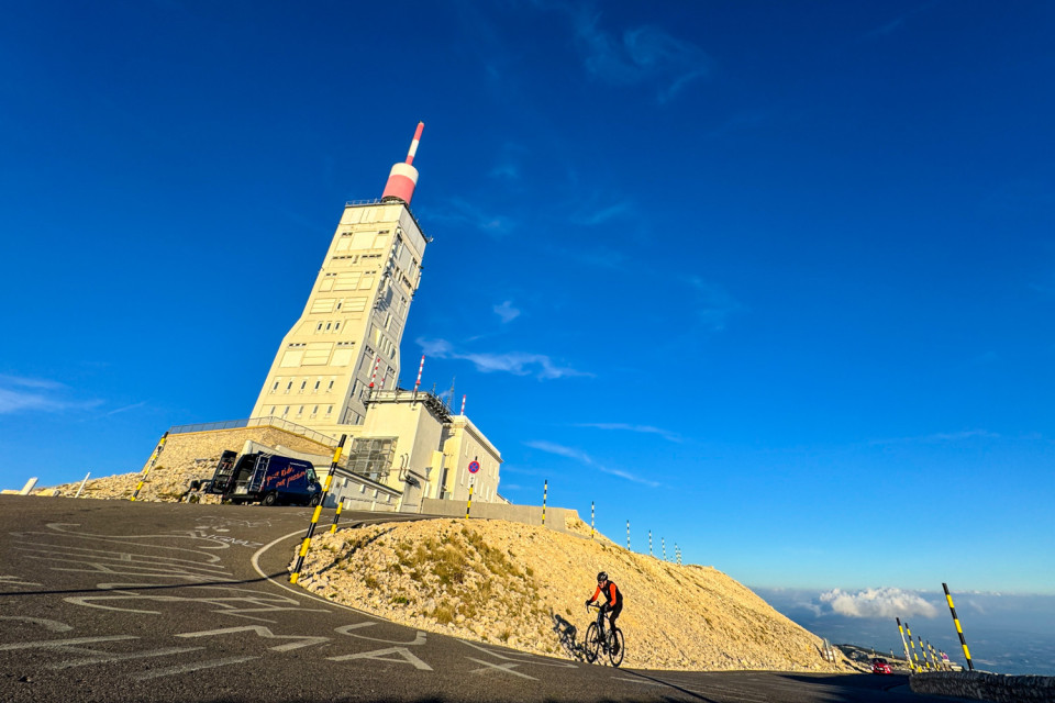 cyclist climbing final hairpin at mont Ventoux summit with marmot tours support vehicle and weather beacon nearby