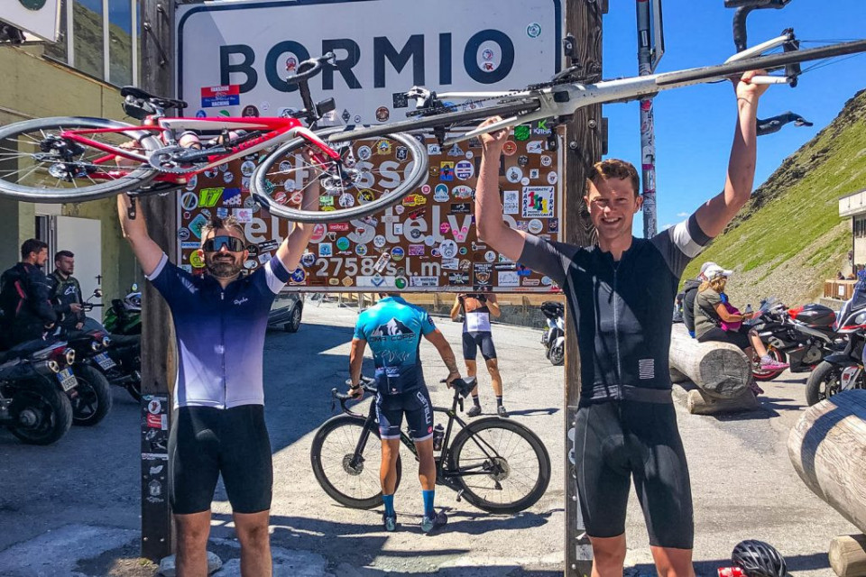 Pair of cyclists holding bikes aloft at Passo dello Stelvio summit on Marmot Tours Raid Dolomites cycling challenge
