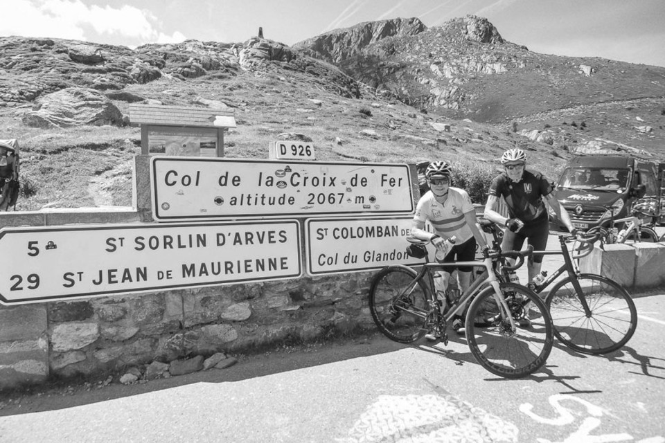 black and white image of two cyclists posing at Croix de for col sign on marmot tours cycling holiday in French alps