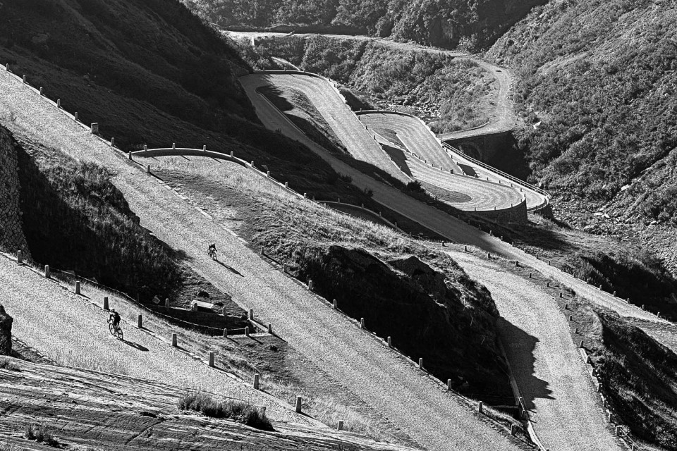 Black and white image of cyclists climbing San Gotthard pass cobbles on Marmot Tours guided road cycling holiday Swiss Alps