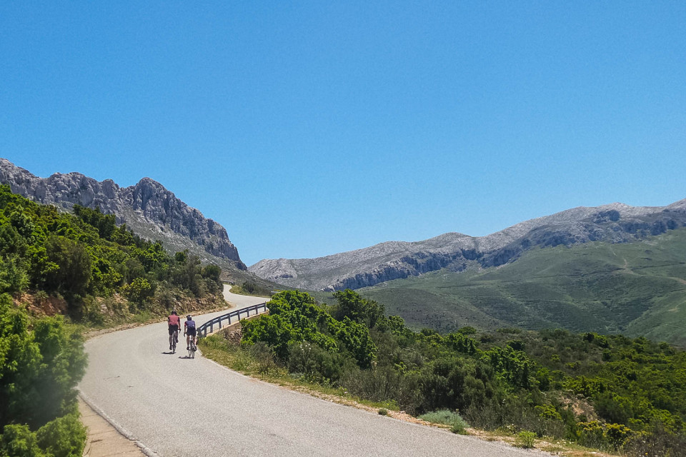 Pair of cyclists climbing through mountains and pastures under blue sky on guided road cycling tour Sardinia with Marmot Tours
