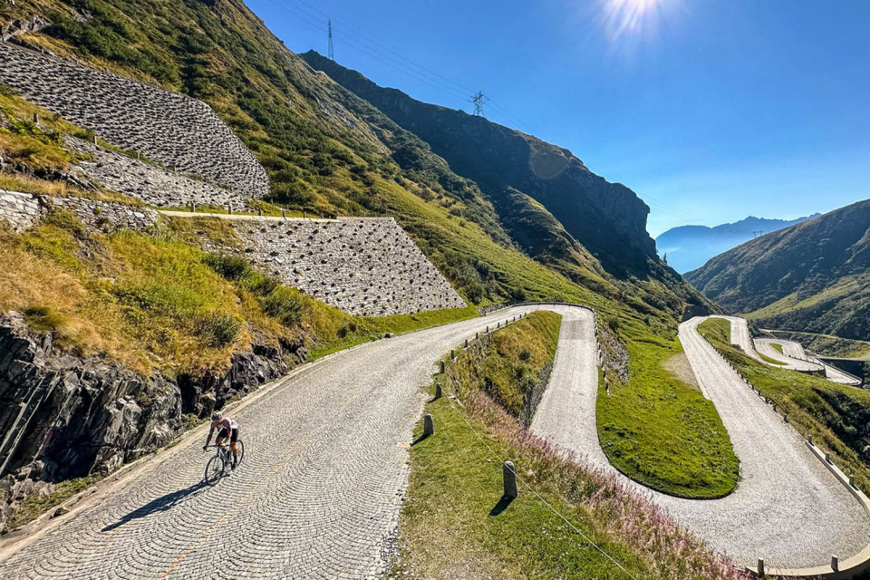 Cyclist climbing cobbles of San Gotthard pass Swiss Alps on Marmot Tours guided road cycling holiday