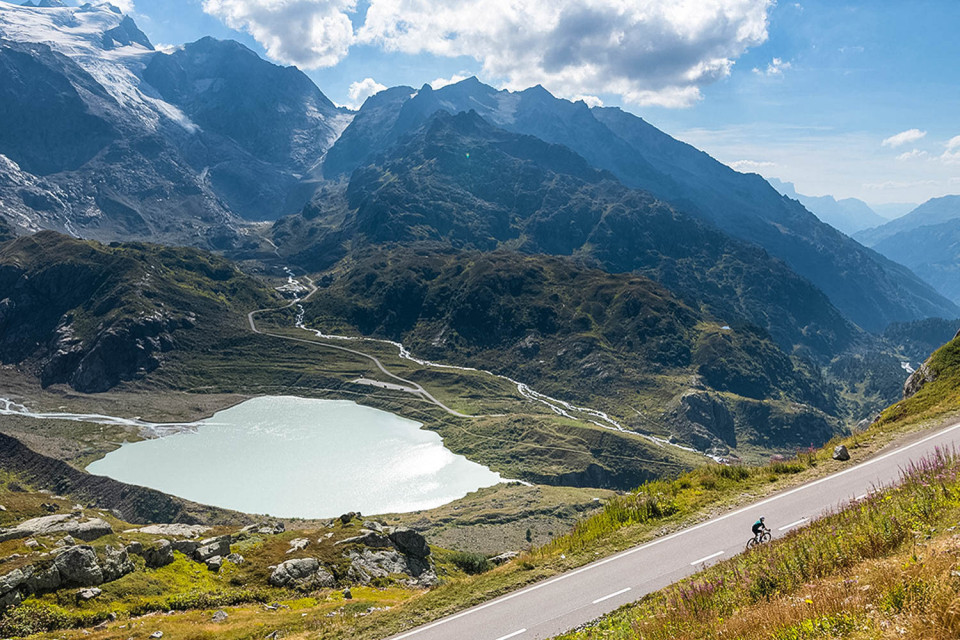 Cyclist climbing sustenpass in Swiss alps alongside glacial lake with mountains in background on marmot tours guided cycling holiday switzerland