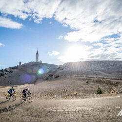 Pair of cyclists rounding hairpin bend climbing Mont Ventoux beneath sunny sky on guided road cycling holiday Provence with Marmot Tours