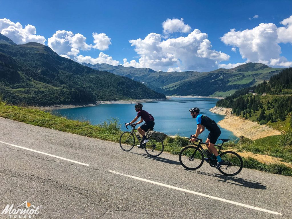 Pair of cyclists climbing in the alps with damn in background with Marmot Tours European road cycling holidays