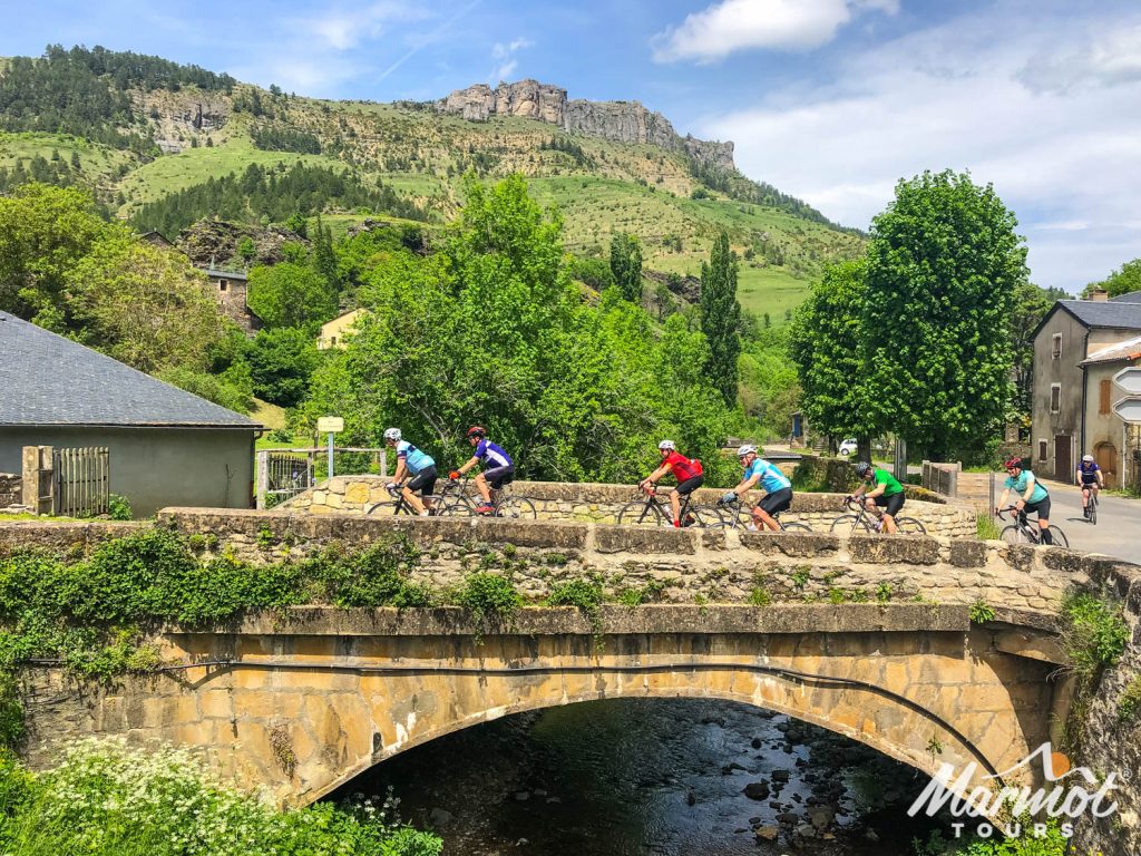 Group of cyclists riding over a bridge in pretty French village on Marmot Tours fully supported road cycling holiday in Cévennes and Ardeche South of France