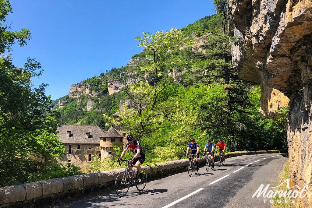 Group of cyclists beneath rock overhang with chateau in rear on Marmot Tours fully supported cycling holiday in South of France Cevennes and Ardeche