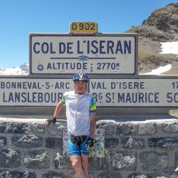 Cyclist smiling at Col de L'Iseran sign on Marmot Tours Raid Alpine cycling challenge
