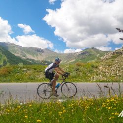 Cyclist climbing on sunny day in mountains on Marmot Tours Raid Alpine cycling challenge