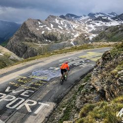 Cyclist climbing mountains with moody sky on Marmot Tours Raid Alpine cycling challenge
