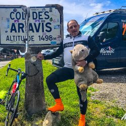 Cyclist smiling with Marmot mascot at Col d'Aravis on Marmot Tours guided road cycling challenge Raid Alpine