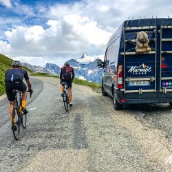 Pair of cyclists climbing with Marmot Tours support vehicle on Raid Alpine cycling challenge