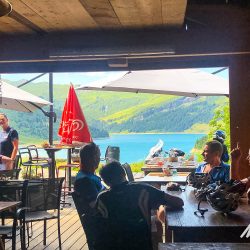 Group of cyclist enjoying cafe rest break with view of Lac Roselend on Marmot Tours guided cycling tour of French Alps