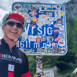 Cyclist smiling at Vrsic Pass sign on Slovenia road cycling holiday with Marmot Tours