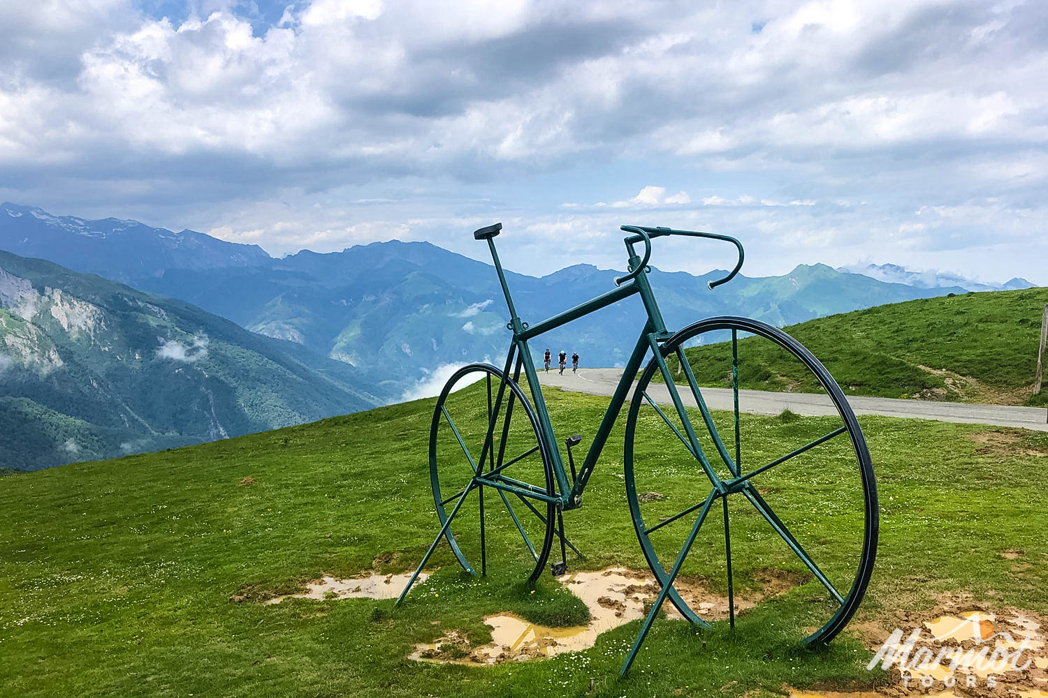 Col d'Aubisque bicycle sculpture with three cyclists and mountain backdrop with Marmot Tours Raid Pyrenean cycling holiday
