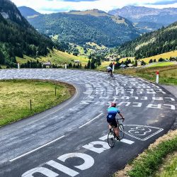 Pair of cyclists descending road covered in Tour de France graffiti on Aravis climb with Marmot Tours guided road cycling holidays French Alps