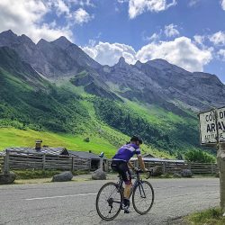Cyclist Alpine peaks and blue sky alongside Col des Aravis col sign with Marmot Tours guided road cycling holidays