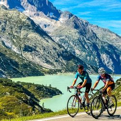Pair of cyclists climbing next to lake on Marmot Tours guided road cycling tour Swiss Alps