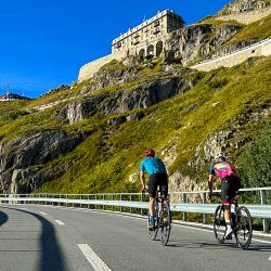 Pair of cyclist climbing Furka pass in Swiss Alps beneath Hotel Belvedere with Marmot Tours guided road cycling holidays