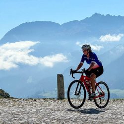 Female cyclist on cobbles of San Gotthard pass Swiss Alps on Marmot Tours road cycling holiday