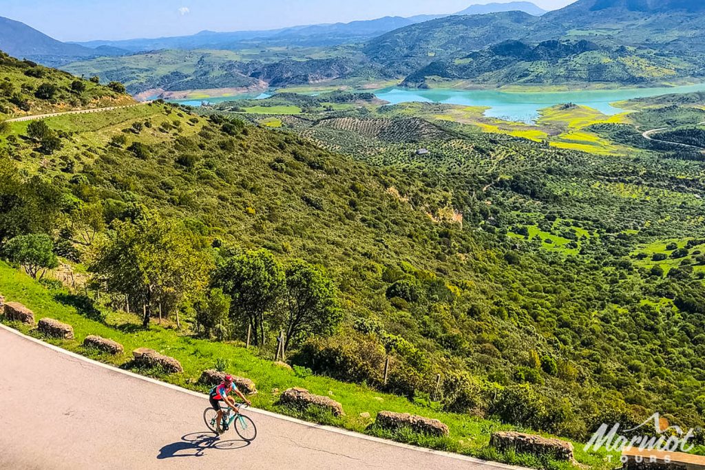 Cyclist surrounded by green landscape and turquoise reservoir on road cycling holiday Andalusia Spain with Marmot Tours
