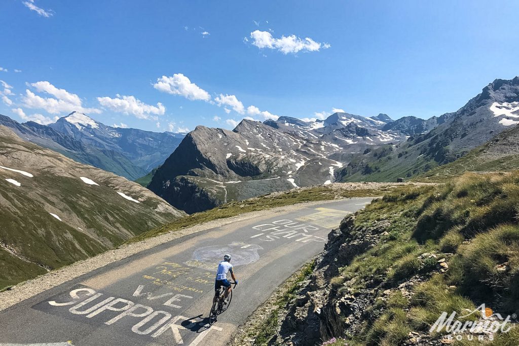 Cyclist on tough climb with mountain peaks in distance on Marmot Tours Raid Alpine cycling challenge