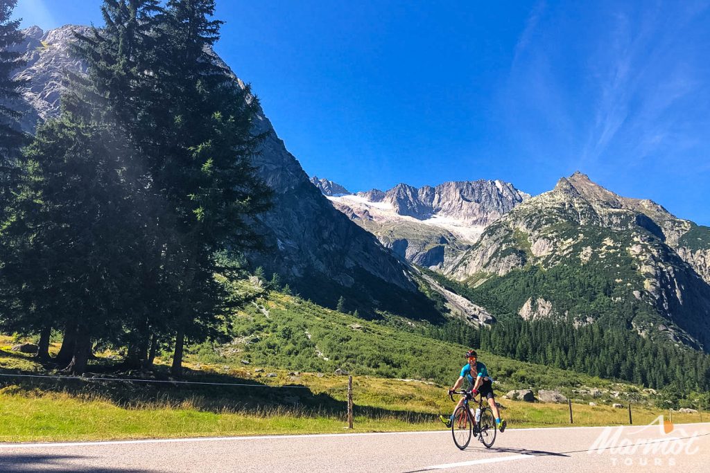 Cyclist riding with feet out of pedals and big grin with Swiss Alps backdrop on Marmot Tours guided road cycling holiday Switzerland