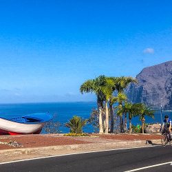 Cyclist on coast road with colourful boat and blue sea on guided road cycling holiday Tenerife with Marmot Tours