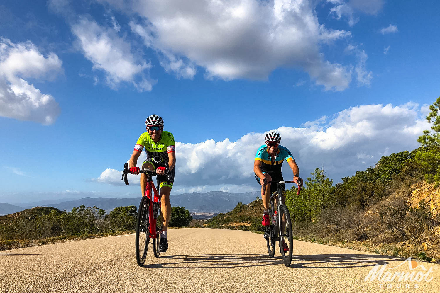 Pair of cyclists and mountain backdrop on sunny day on Marmot Tours full support cycling holiday in Sardinia