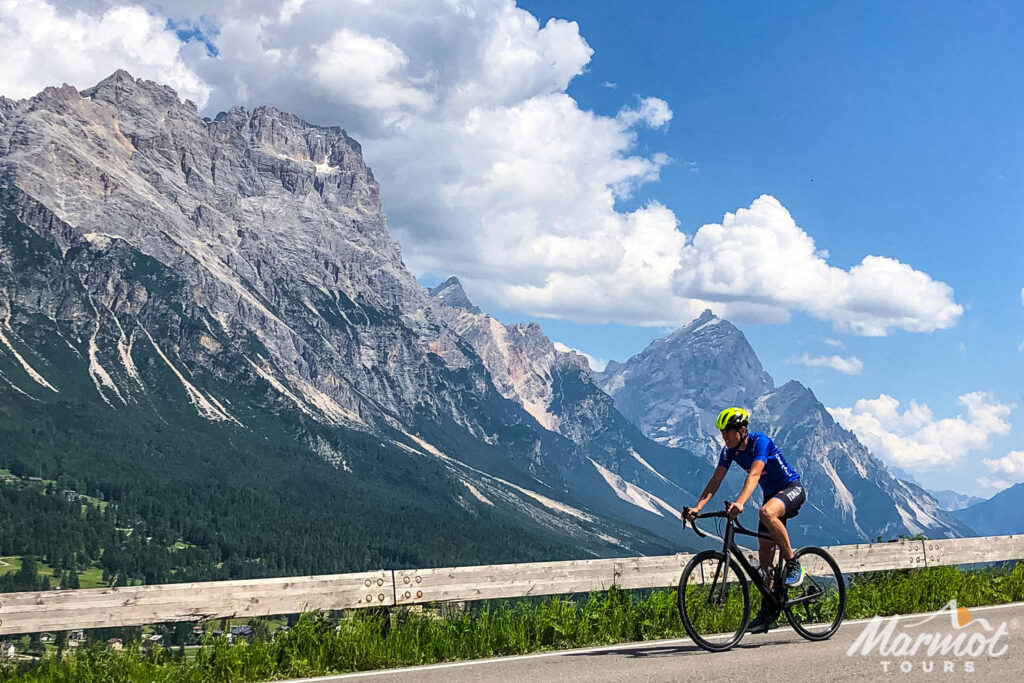 Cyclist descending mountain road with Dolomites backdrop on sunny day with Marmot Tours guided road cycling holidays in Italian Dolomites cycling Italian Alps