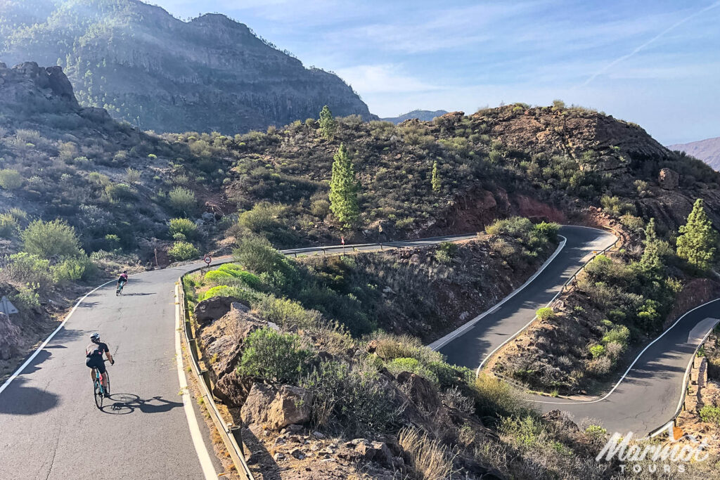 Cyclists descending Pico de las Nieves climb Gran Canaria with multiple hairpins beneath blue skies on full support cycling holiday with Marmot Tours