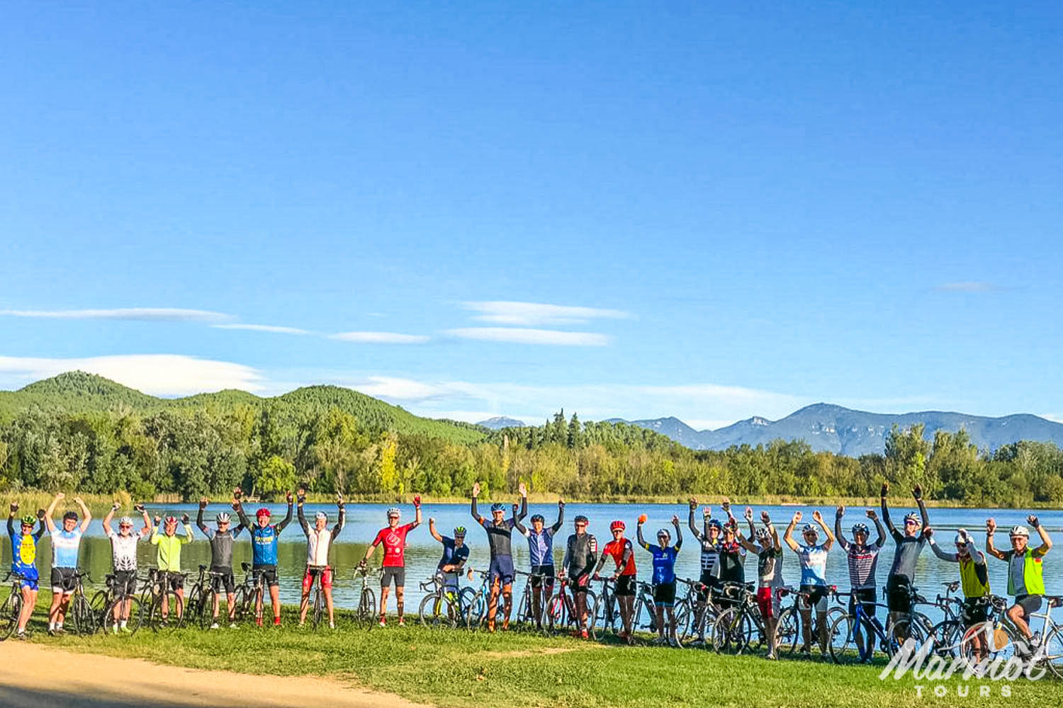 Group of cyclists cheering on the shore of Lake Bangles on guided road cycling tour Catalonia and Girona with Marmot Tours